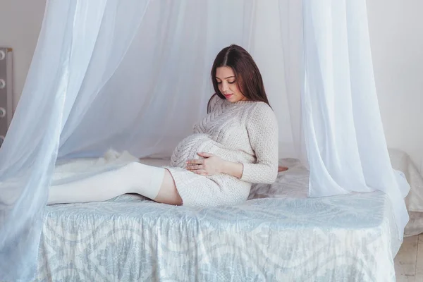 Güzel bir hamile kadın bebek bekliyor. Gölgelik ile yatakta oturuyor. Annelik kavramı. — Stok fotoğraf