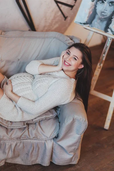 Fille brune enceinte dans un pull tricoté blanc couché dans un fauteuil . — Photo