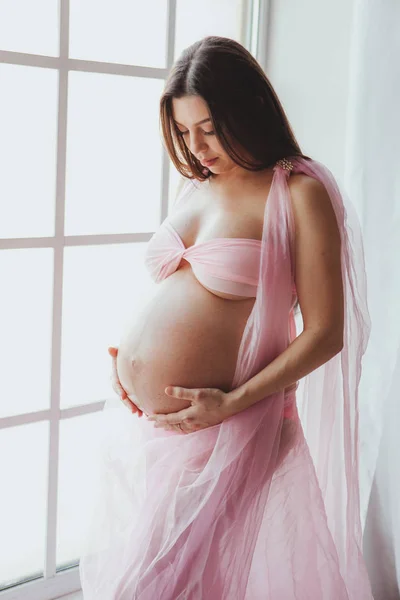 Retrato de close-up de jovem grávida beleza tenra em pé na frente da janela e tocando sua barriga em casa. Loft interior minimalista — Fotografia de Stock