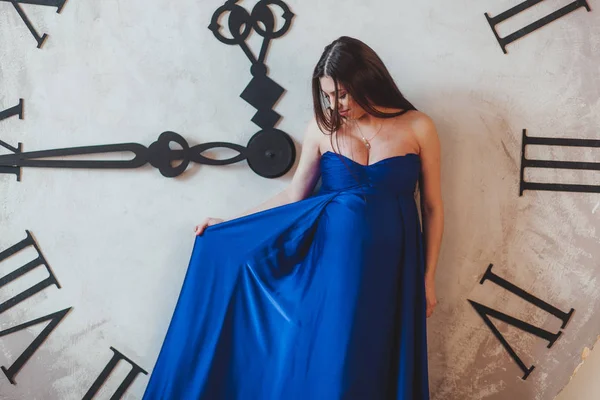 Uma mulher grávida em um belo vestido longo azul em pé na frente de um relógio enorme — Fotografia de Stock