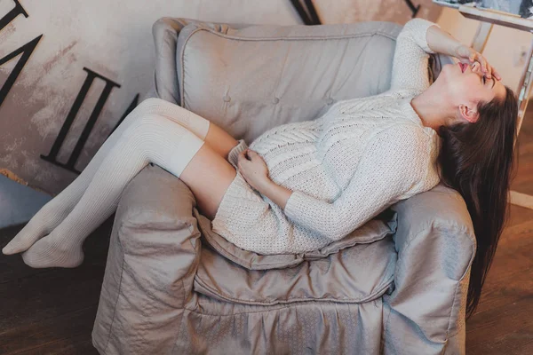 Brunetka dziewczyna w ciąży w biały sweter z dzianiny, leżącego w fotel. — Zdjęcie stockowe