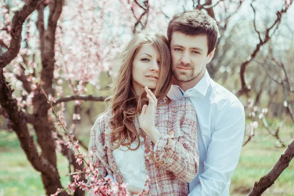 Giovane coppia felice ed elegante innamorata che si abbraccia nel giardino fiorito. Ragazzo e ragazza che riposano all'aperto . — Foto Stock