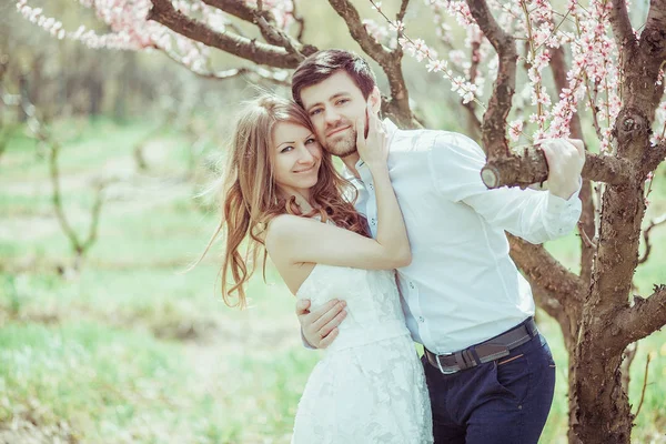 Ritratto di una coppia felice sorridente: bel giovane uomo che tiene bella giovane donna all'aperto in una luminosa giornata di sole di primavera o estate nel giardino di fiori di melo verde . — Foto Stock