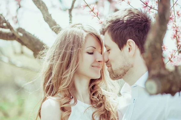 Young and happy newlyweds are touching noses in blooming park. Close-up outdoor portrait — Stock Photo, Image