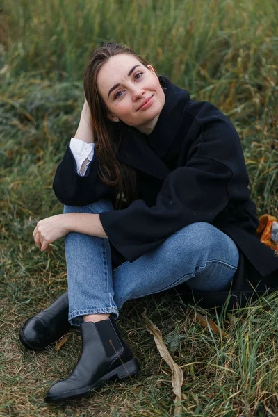 Belle jeune femme posant en souriant sur un paysage d'herbe pittoresque. Mode de vie décontracté vêtements jeans et manteau — Photo