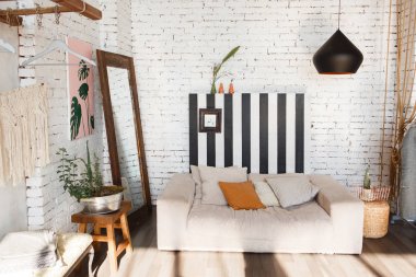 Modern çatı iç kanepe, stüdyo lambası, ayna, çizgili beyaz tuğla duvar ve çiçekler tencerede ile.