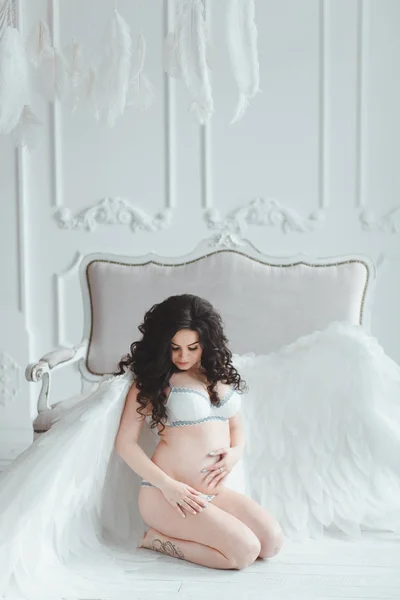 Menina grávida bonita com grandes asas de anjo no estúdio branco. Sentado no chão — Fotografia de Stock