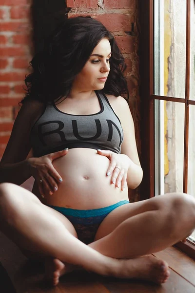 Junge schwangere Frau sitzt auf der Fensterbank — Stockfoto