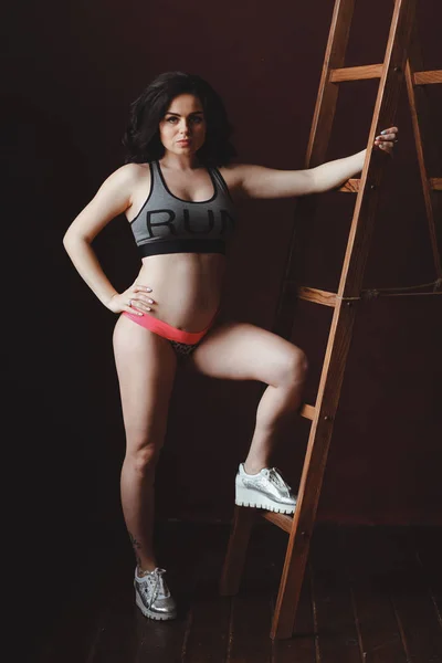 Mulher grávida fazendo exercícios de ginástica no fundo da parede marrom perto da escada . — Fotografia de Stock