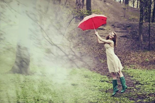 Una donna viene spazzata via con il suo ombrello rosso punteggiato nella foresta. Concetto Mary Poppins — Foto Stock