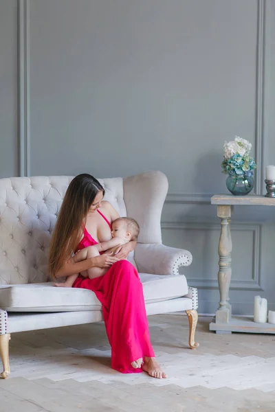 Uma jovem mãe amamentando seu bebê. Mãe a amamentar bebé. Mulher e menino recém-nascido relaxar em uma sala de estar cinza com cadeira de balanço . — Fotografia de Stock