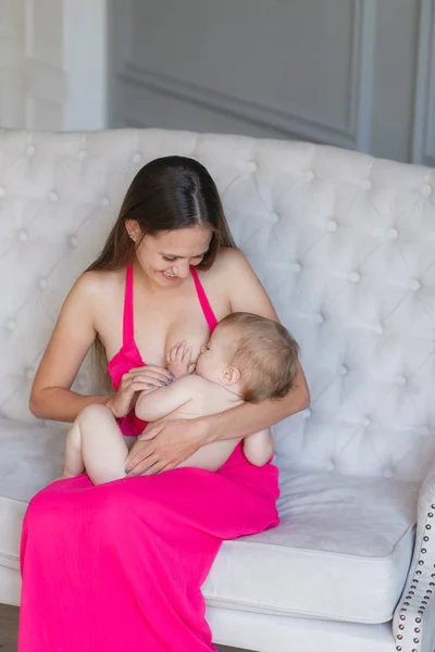 Jovem mulher amamentando seu bebê em casa, close-up. Vestindo vestido rosa . — Fotografia de Stock