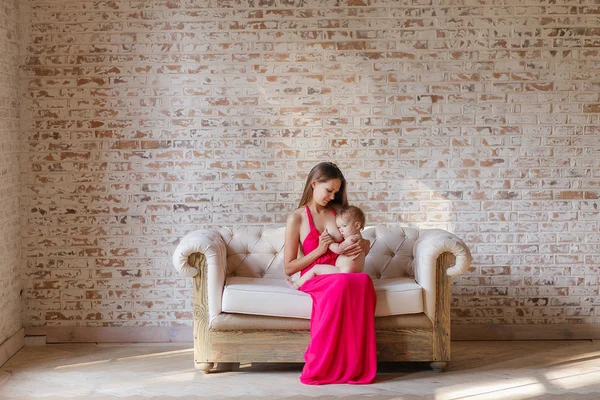 Mãe amamentando bebê sentado no sofá no interior do projeto loft com parede de tijolo no fundo — Fotografia de Stock