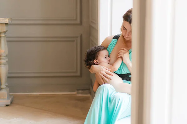 Uma mãe amamentando sua filhinha em seus braços sentada no peitoril da janela — Fotografia de Stock