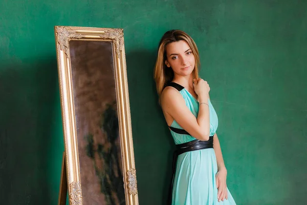 Joven hermosa mujer en vestido de cóctel de pie cerca del espejo vintage. Con la pared vacía verde en el fondo, copyspace — Foto de Stock