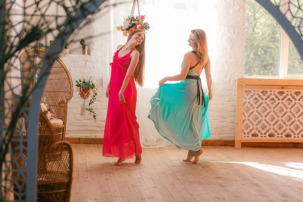 Duas mulheres atraentes dançando em vestidos coloridos pé nu no chão de madeira na sala à moda antiga — Fotografia de Stock
