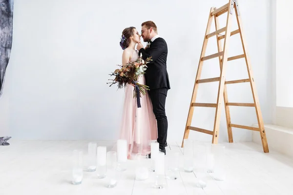 Tender bride and groom standing in white studio with wooden ladder — Stock Photo, Image