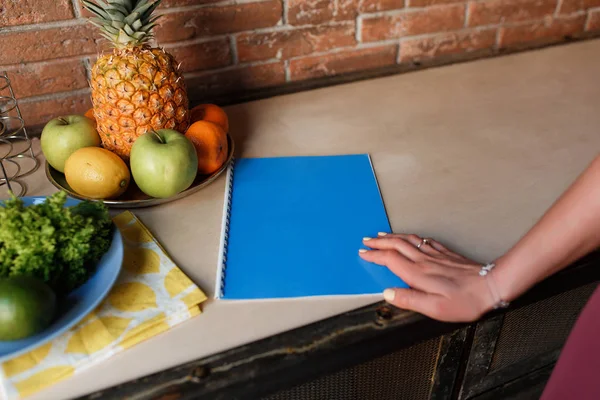 Healthy Food. Woman Hand on blue notebook, kitchen table with pineapple and fruit