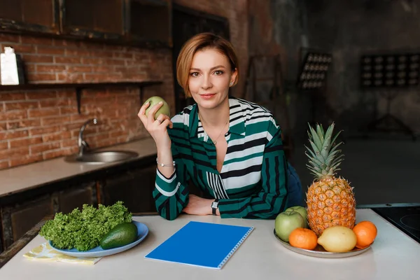 Hermosa mujer joven sana comiendo manzana en su moderna cocina loft. Entrenador. Come bien para mantener tu barriga apretada. — Foto de Stock