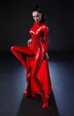 brünette Frau in rotem Latex-Anzug posiert auf dunklem Hintergrund