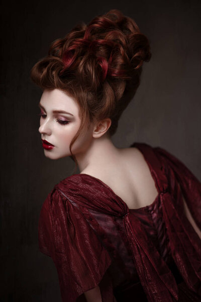 Portrait of redhead woman with baroque hairstyle and evening maroon dress