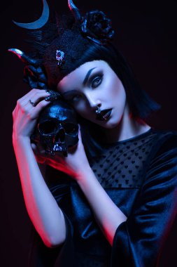 Gotik tarzda siyah elbiseli genç bir kadın kafatasıyla poz veriyor.