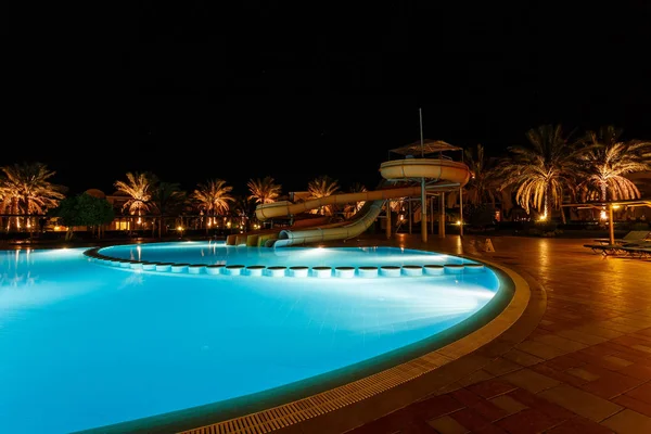 Illuminated pool at night with tropical palms — Stock Photo, Image