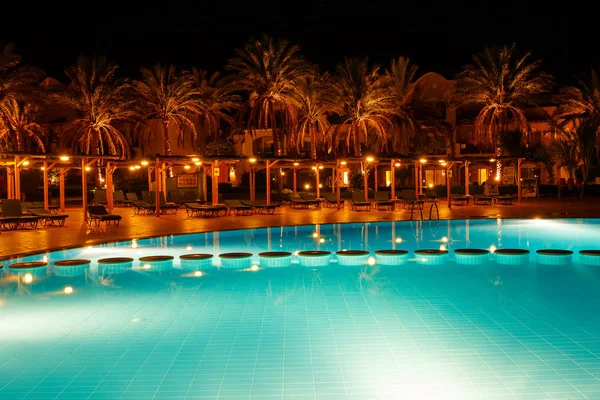 Illuminated pool at night with tropical palms — Stock Photo, Image