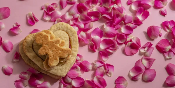 恋人のペアは クッキーとピンクの背景にバラの花びらで作られた心の上にあります — ストック写真