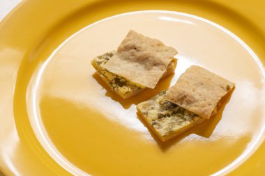 İki dilim peynirli ve otlu turta sarı bir tabakta..