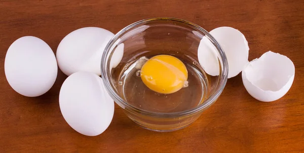 Gebroken ei in een glazen schaal met hele eieren en schelp — Stockfoto