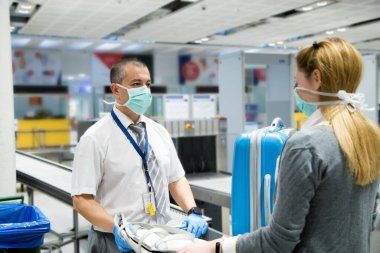 Havaalanı güvenlik görevlisi, koronavirüs pandemisi ihtimaline karşı COVID 19 'u önlemek için mavi eldiven ve maske takıyor.