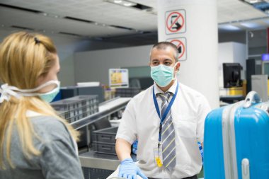 Havaalanı güvenlik görevlisi, koronavirüs pandemisi ihtimaline karşı COVID 19 'u önlemek için mavi eldiven ve maske takıyor.