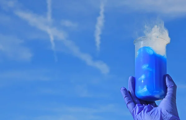 White smoke comes from a beaker with blue solution of fluoresceine after addition of dry ice. Chemist demonstration experiment.