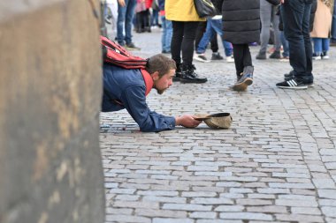 PRAGUE, CZECH REPUBLIC - October 30, 2019: oung man asking for alms on the background of the feet of passersby at the exit of Charles Bridge. Deadline or profession.