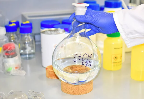 Large round-bottom flask flask with ethanol in the hands of an employee of the laboratory on the background of the working surface. Alcohol. Spirit.