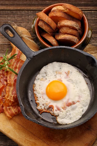 Fried egg with hot bacon pieces in a cast iron skillet — Stock Photo, Image