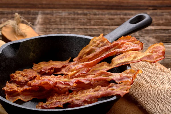 Hot stekt bacon bitar i en stekpanna i gjutjärn — Stockfoto