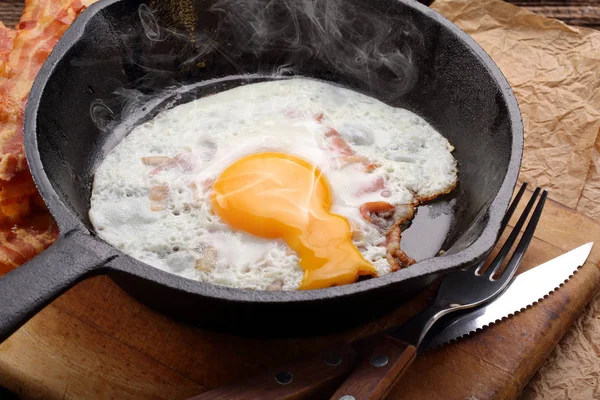 Жареное горячее яйцо с кусочками горячего бекона в чугунной сковороде — стоковое фото