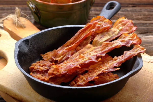 Hot stekt bacon bitar i en stekpanna i gjutjärn — Stockfoto