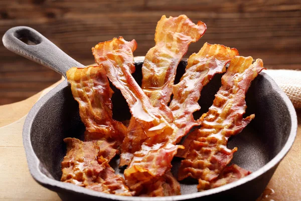 Hot stekt bacon bitar i en stekpanna i gjutjärn — Stockfoto