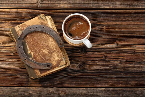 Старая книга, ржавая подкова и чашка кофе на деревянном фоне — стоковое фото