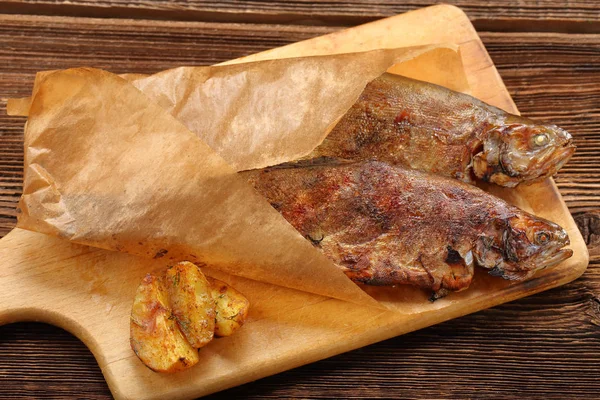 Ryba pieczona z ziemniakami, zawinięte w papier na podłoże drewniane — Zdjęcie stockowe