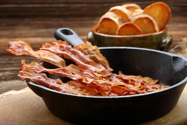 Trozos de tocino frito caliente en una sartén de hierro fundido — Foto de Stock