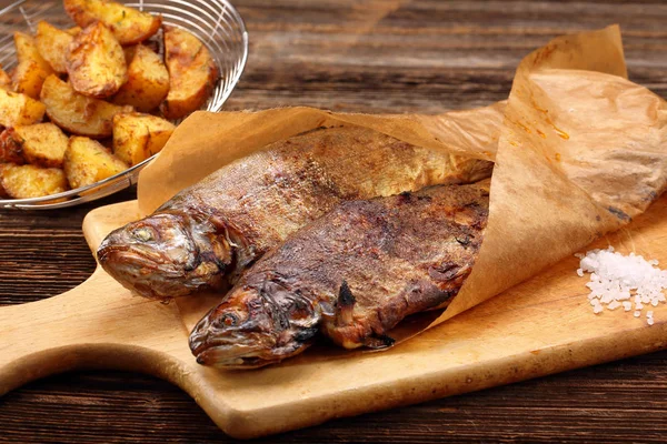 Peixe grelhado com batatas embrulhadas em papel sobre fundo de madeira — Fotografia de Stock