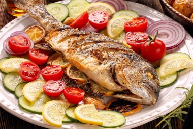 Ahşap arka planda sebzeli kızarmış dorada balığı.