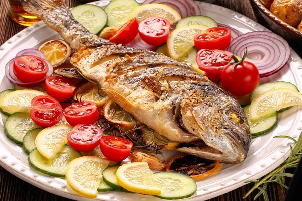 Ahşap arka planda sebzeli kızarmış dorada balığı.