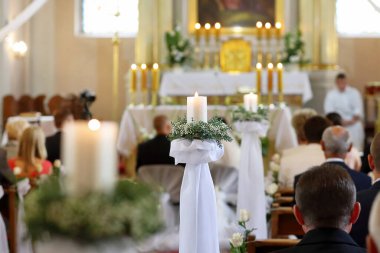 Kilisedeki düğün süslemeleri, genç bir çift ve arka gruptaki misafirler.