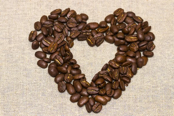 Heart made with coffee beans stacked against burlap canvas — Stock Photo, Image