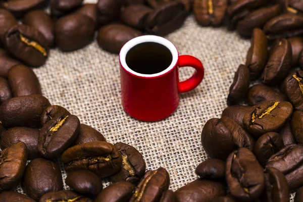 Corazón de granos de café y una taza sobre fondo de arpillera —  Fotos de Stock